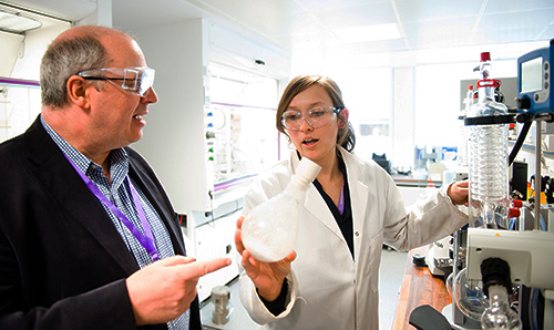 Female researcher wearing white lab coat discussing experiment with man in suit