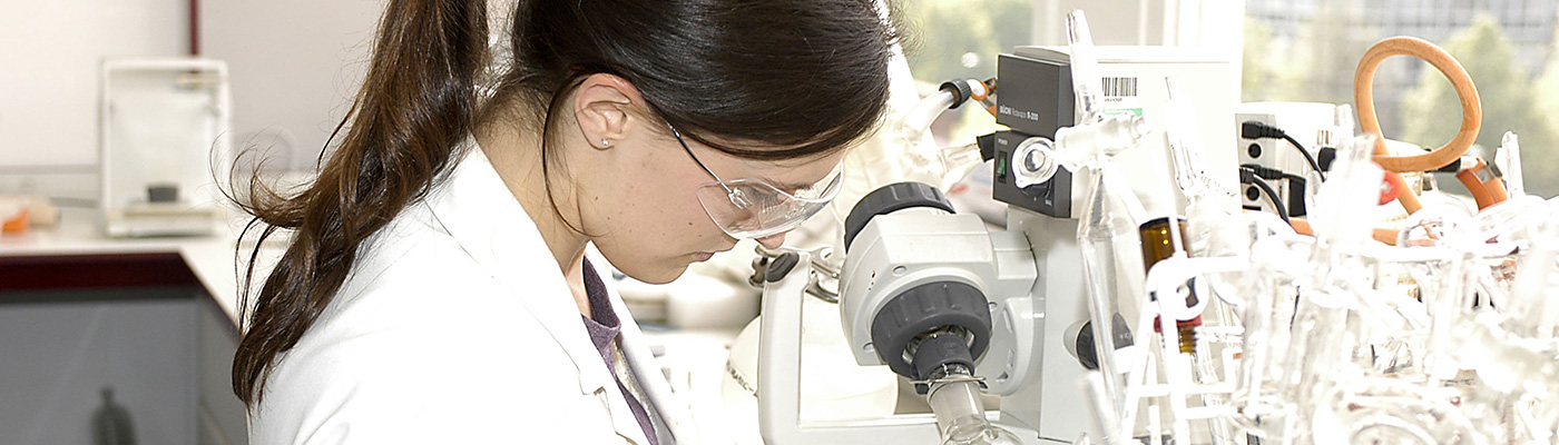 Female researcher in white lab coat looking through lab equipment