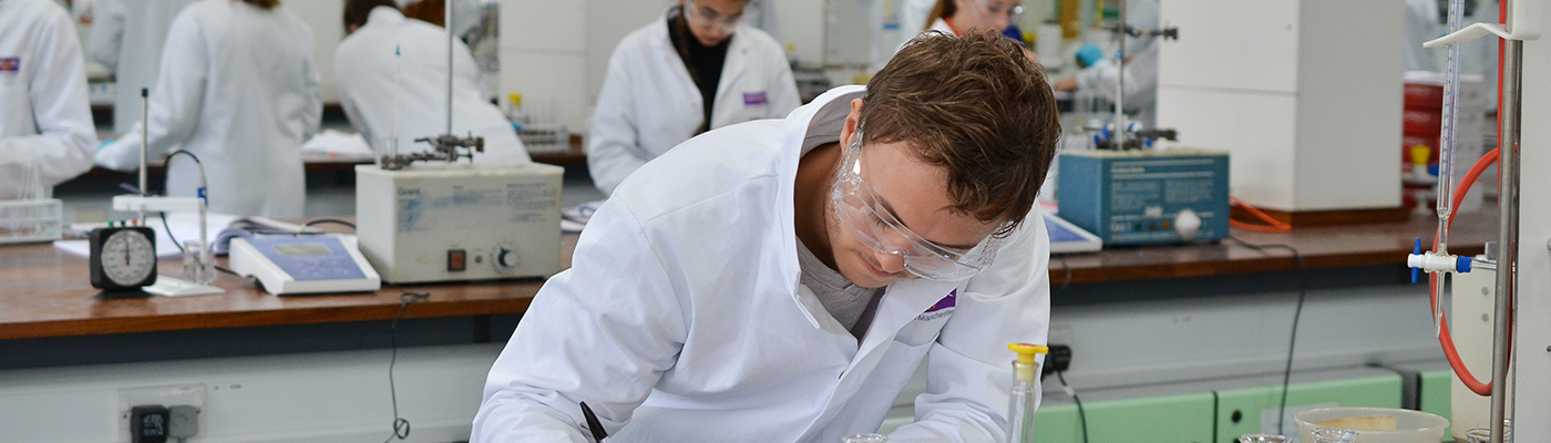 A male researcher in a lab coat with his head down writing