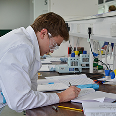 A male researcher in lab coat writing down notes