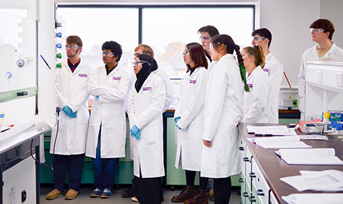 A number of students in lab coats watching a demonstration