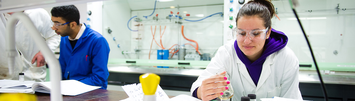 Female student in safety glasses examining a solution in a beaker