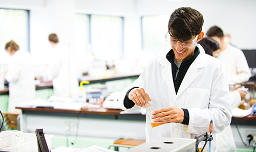 A male researcher in a lab coat smiling down at his experiment