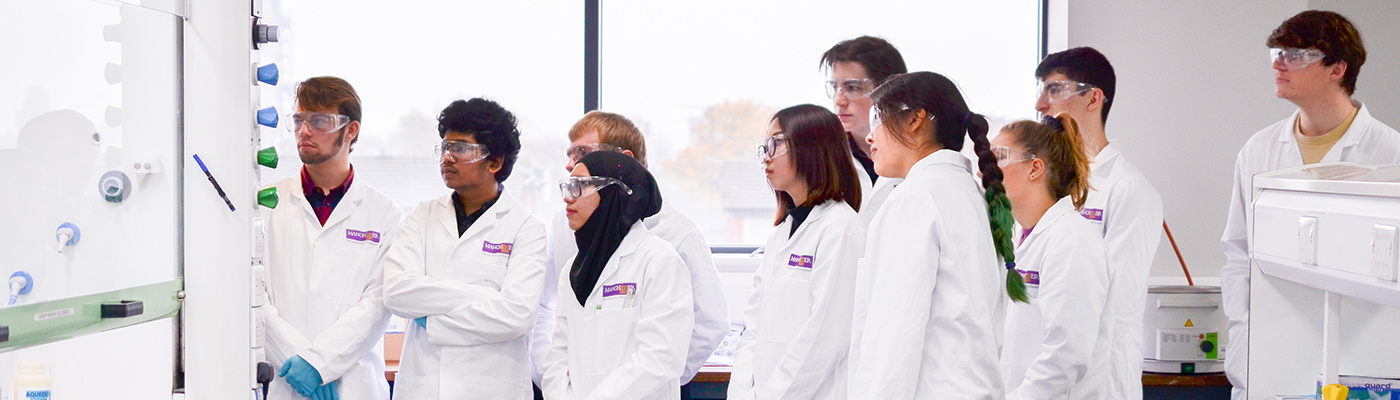 A group of students in lab coats watching a demonstration