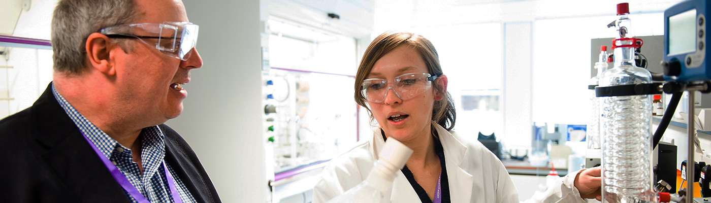 Female researcher in white coat discussing experiment with man in suit