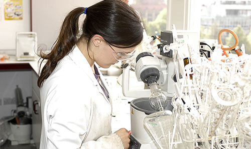 Female researcher in white lab coat looking through lab equipment