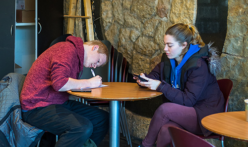 Two students in the Chemistry Cafe; one looking at her smartphone