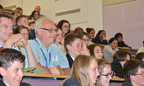 Academics and school students observing something off camera in a lecture theatre