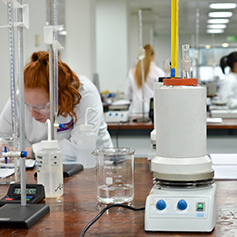 A female researcher in lab coat and glasses, as well as various bits of equipment
