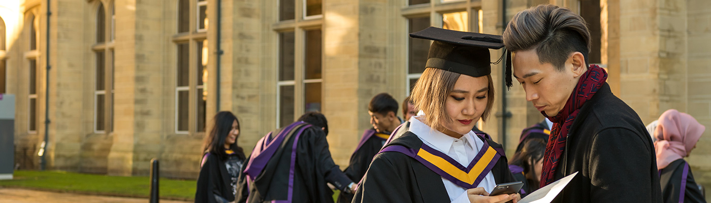 A student in her graduation gown checking her phone with a friend