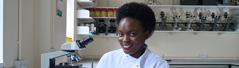 Female student wearing lab coat smiling at camera in laboratory