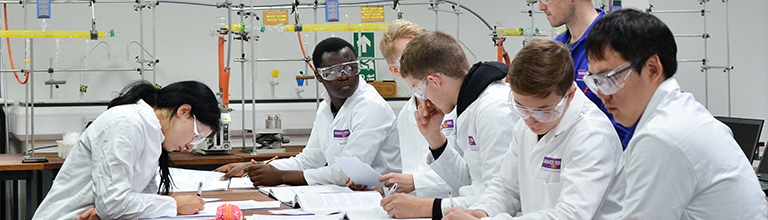 A group of students in lab coats sat down discussing their work