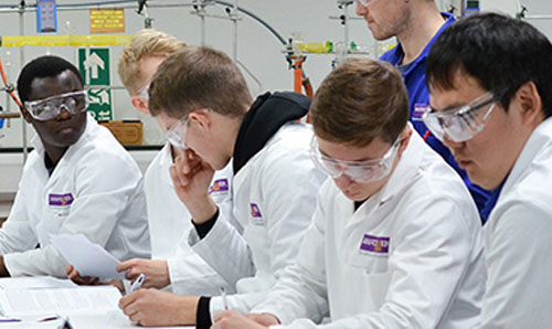 A group of students in lab coats working together at a desk